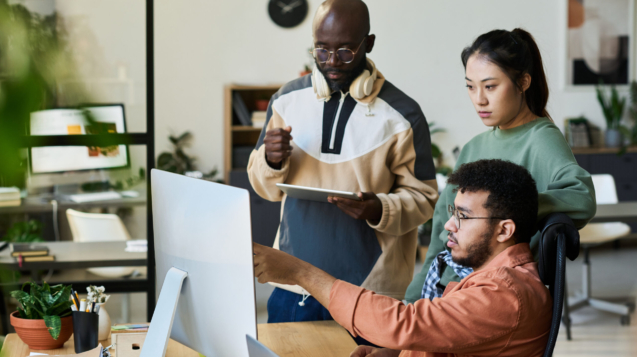 Group of young colleagues looking at screen of desktop computer while one of them pointing at new software product